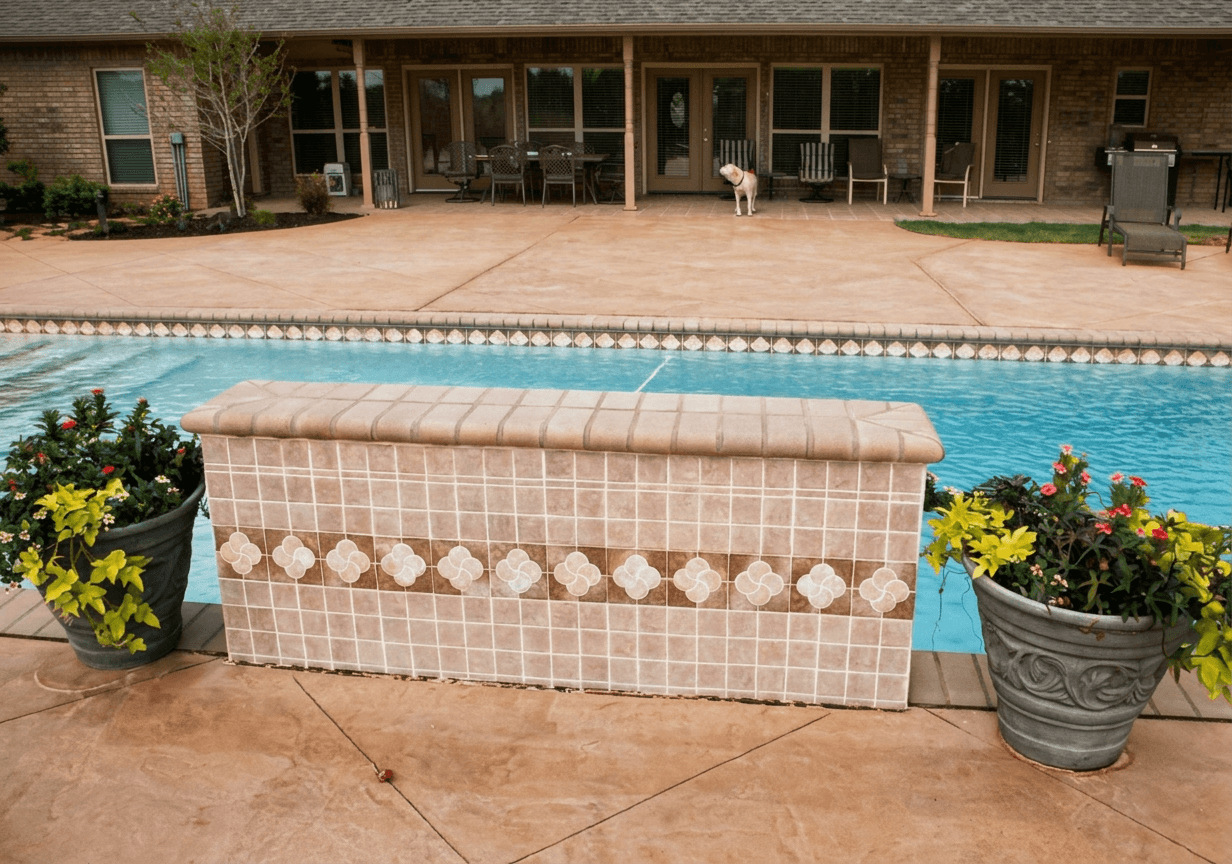 Rectangular pool with raised tiled spillover spa wall, stamped concrete deck, and brick home patio